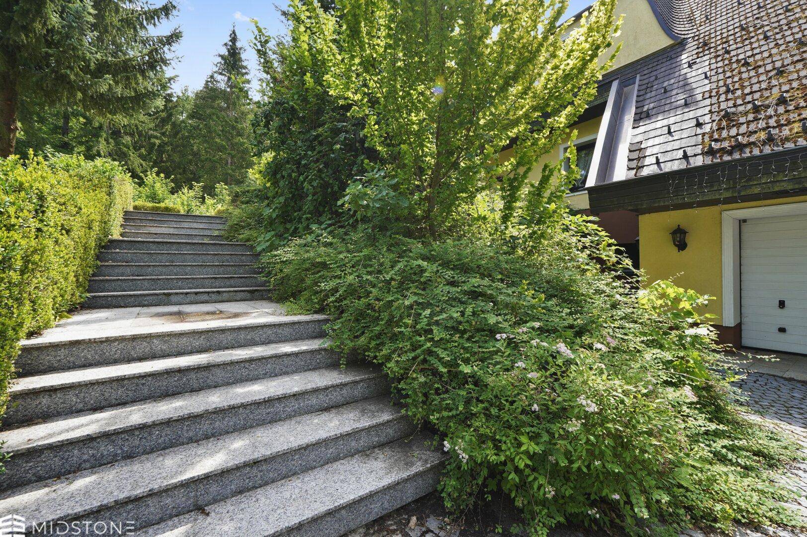 Steintreppe führt durch üppiges Grün zum Eingang des Hauses.