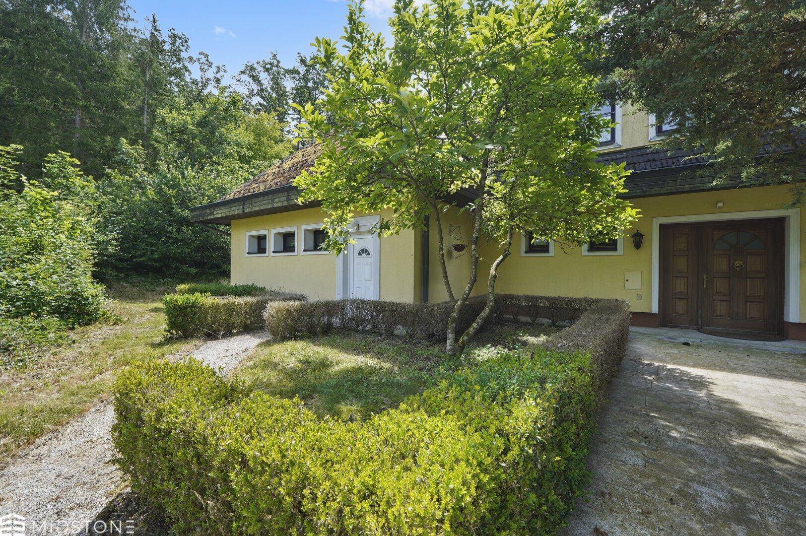 Seitenansicht des Hauses mit kleinem Gartenbeet, Hecken und einer weißen Nebentür.