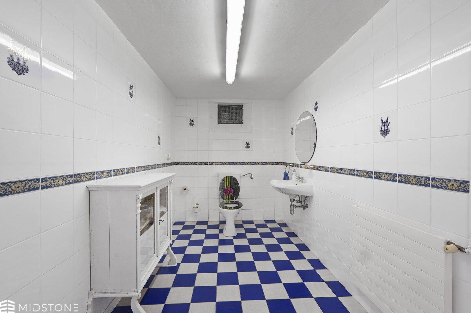 Badezimmer mit blau-weiß karierten Bodenfliesen, weißen Wandfliesen und einem Einzelwaschbecken.