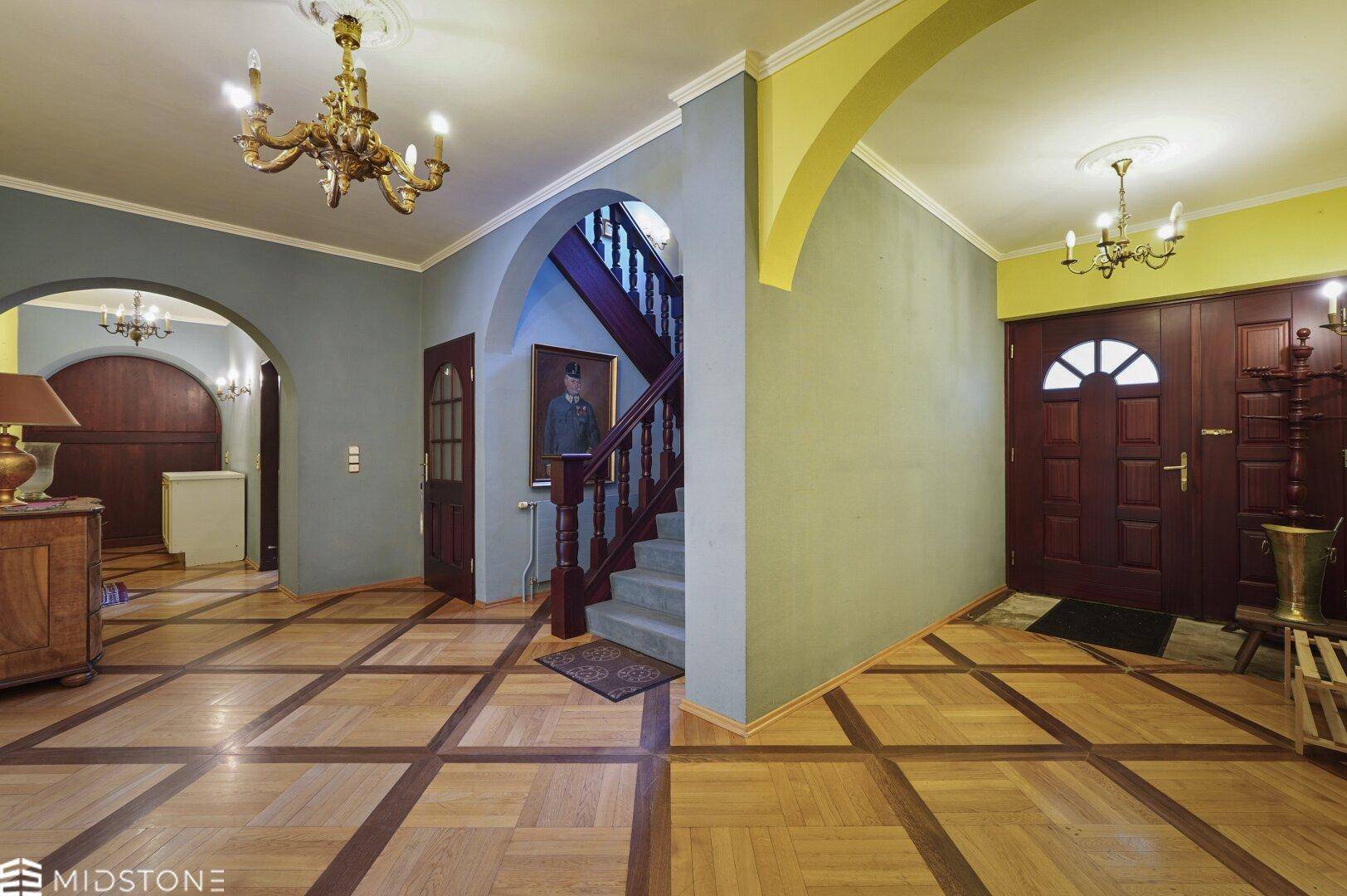 Geräumiger Flur mit Parkettboden, farbigen Wänden und einer eleganten Holztreppe.