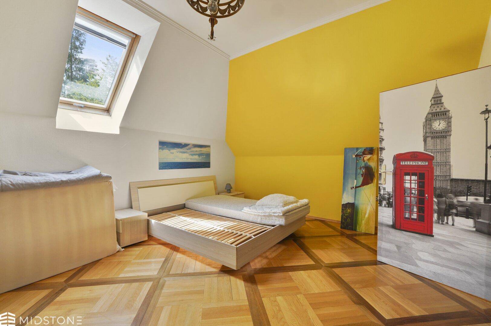 Helles Schlafzimmer im Dachgeschoss mit Dachfenster, Holzbalkendecke und Parkettboden.