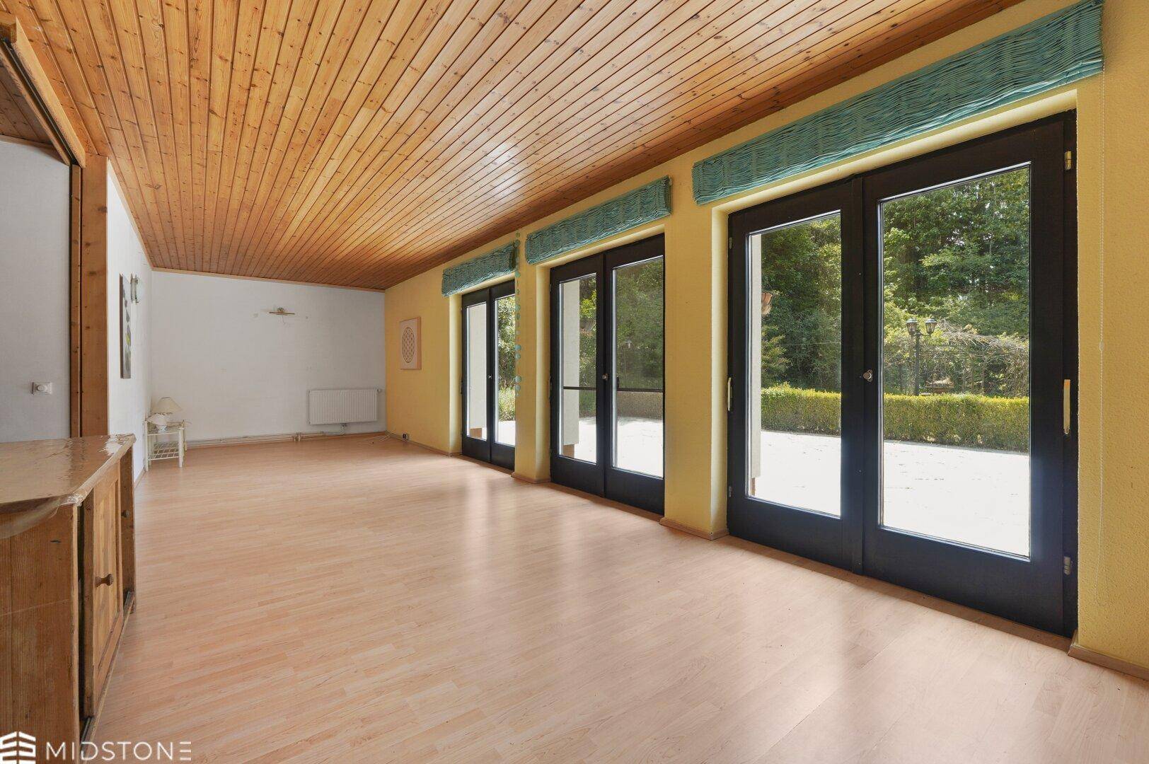 Großer, heller Raum mit Holzdecke und mehreren Glastüren zum Garten.