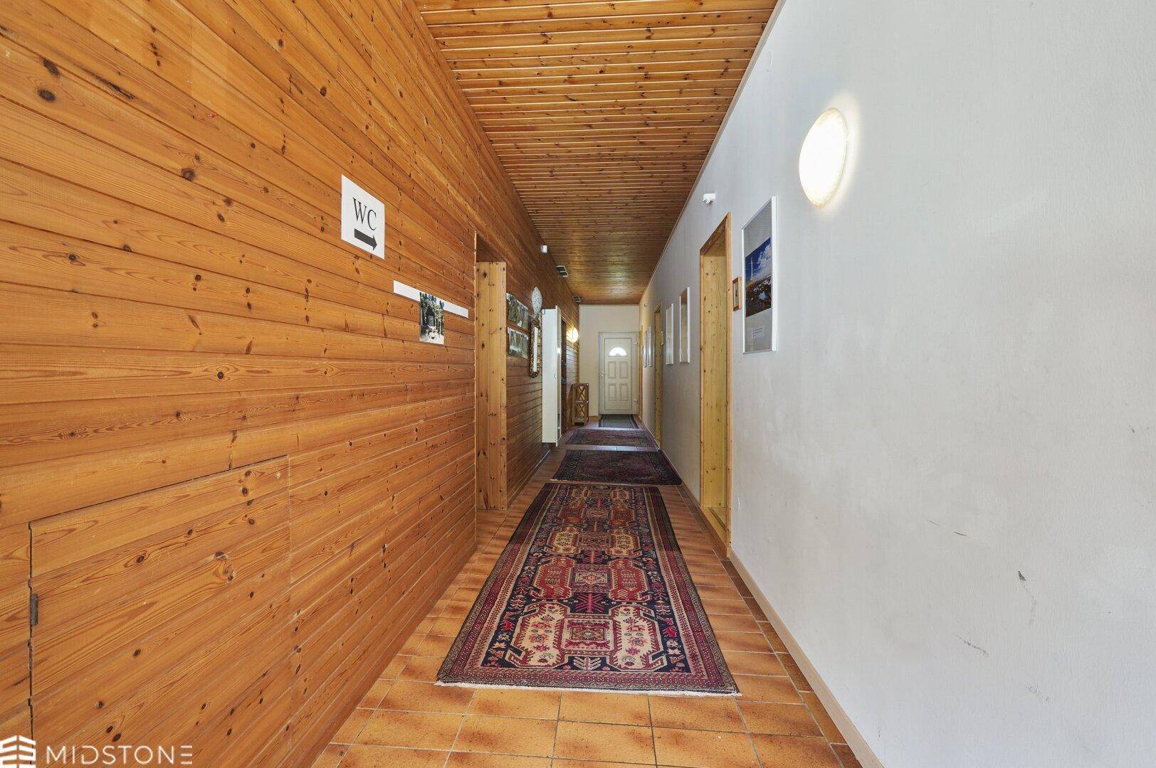 Langer Flur mit Holzvertäfelung, Teppichläufer und Zugang zu verschiedenen Räumen.