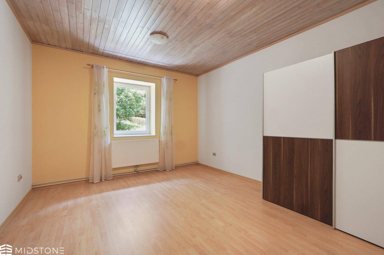 Helles Schlafzimmer mit Holzdecke, Laminatboden und großem Kleiderschrank.