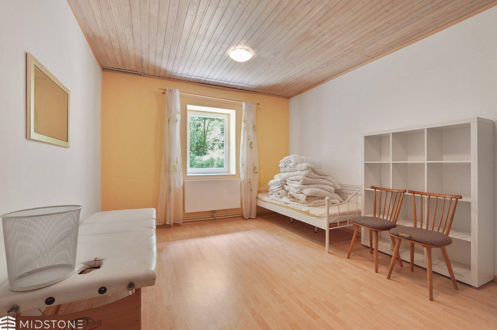 Schlafzimmer mit Holzdecke, Laminatboden und Fenster mit Blick ins Grüne.
