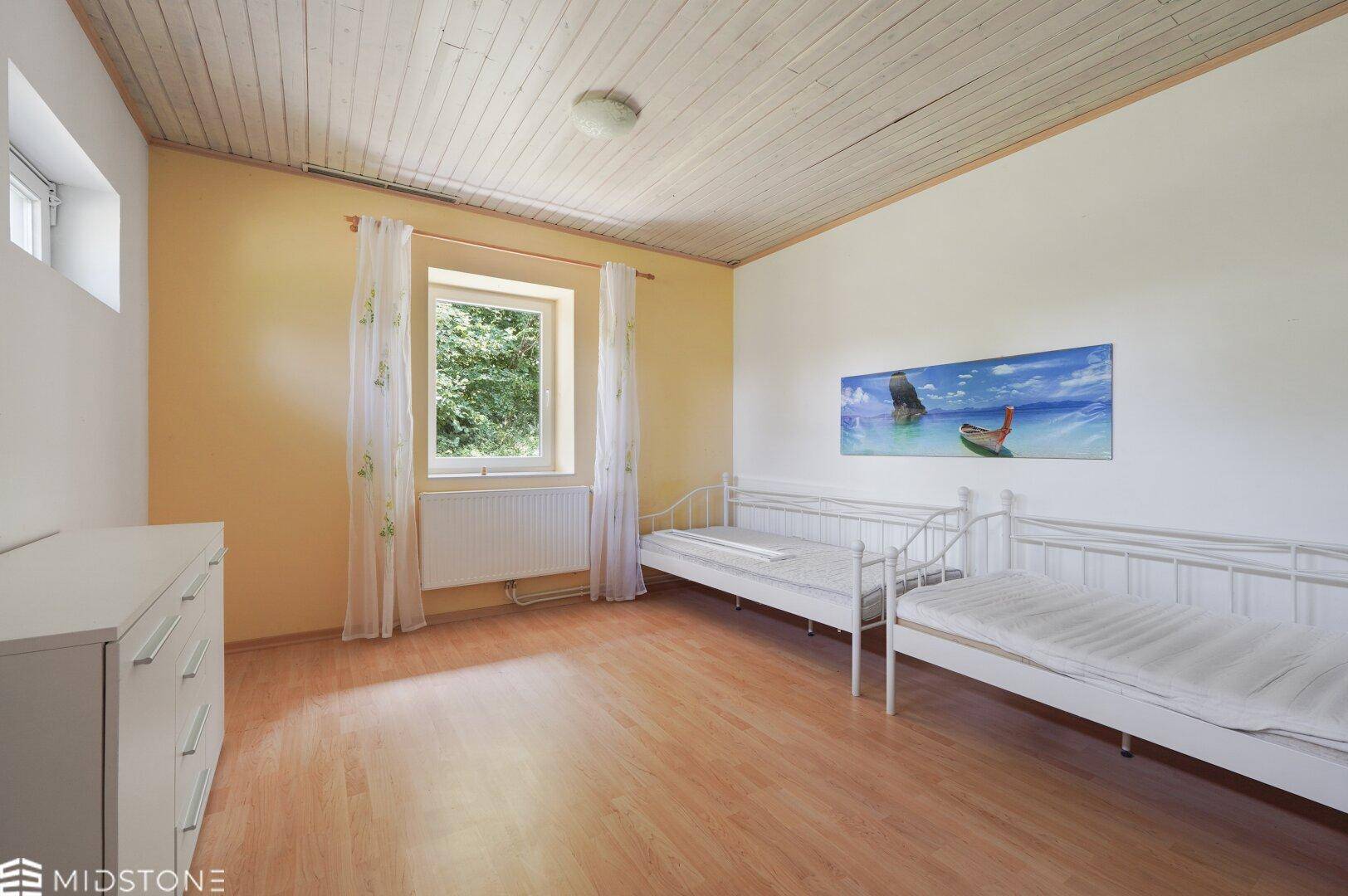 Geräumiges Schlafzimmer mit zwei Betten, Laminatboden und Fenster mit Blick ins Grüne.