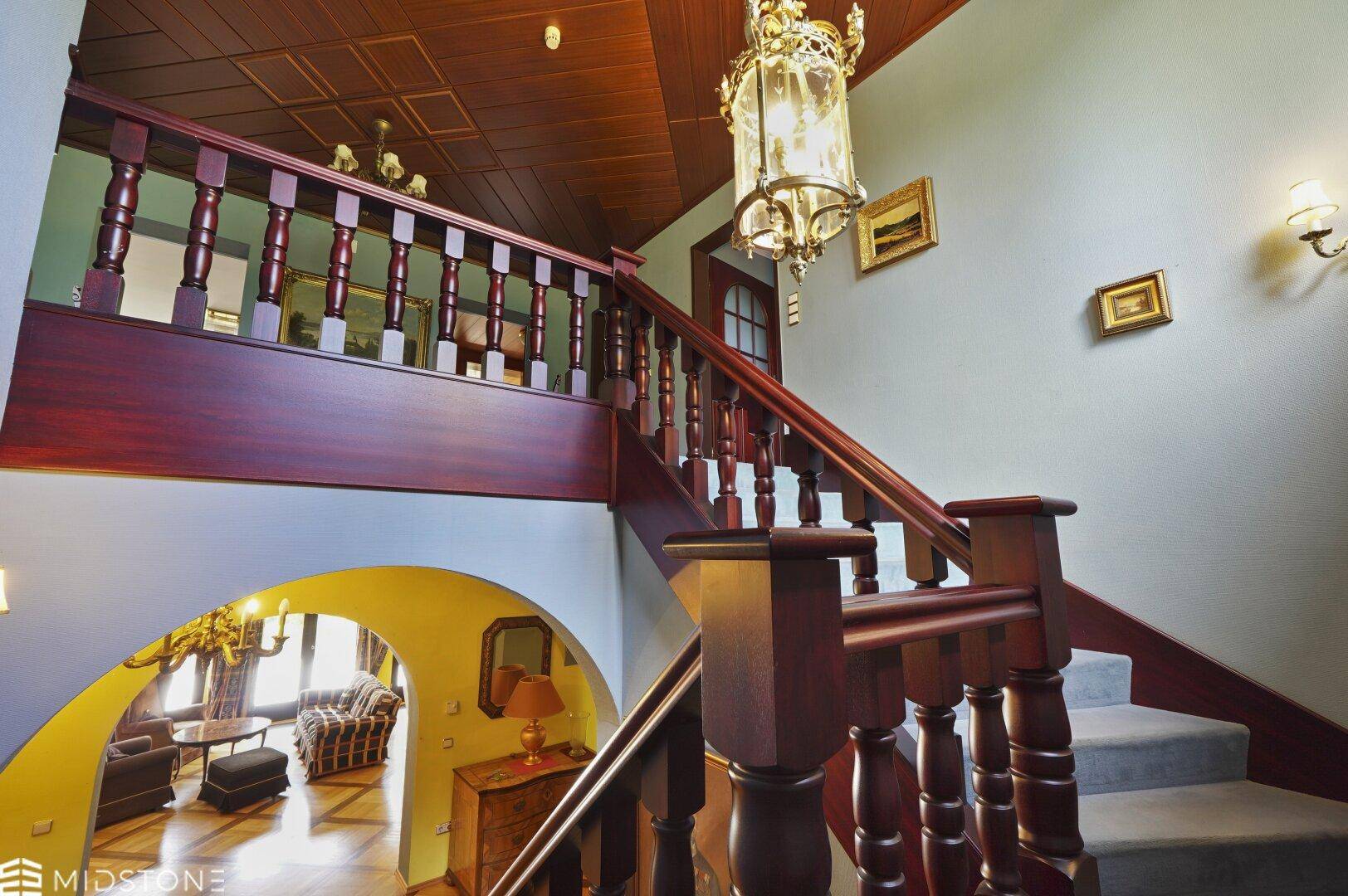 Elegantes Treppenhaus mit dunklem Holzgeländer und Teppichstufen, führt zu den oberen Etagen.
