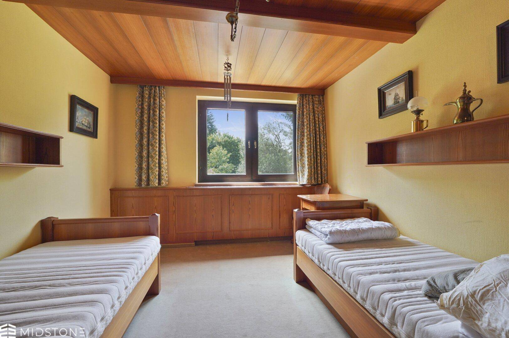 Helles Schlafzimmer mit zwei Einzelbetten, Holzdecke und eingebauten Regalen.
