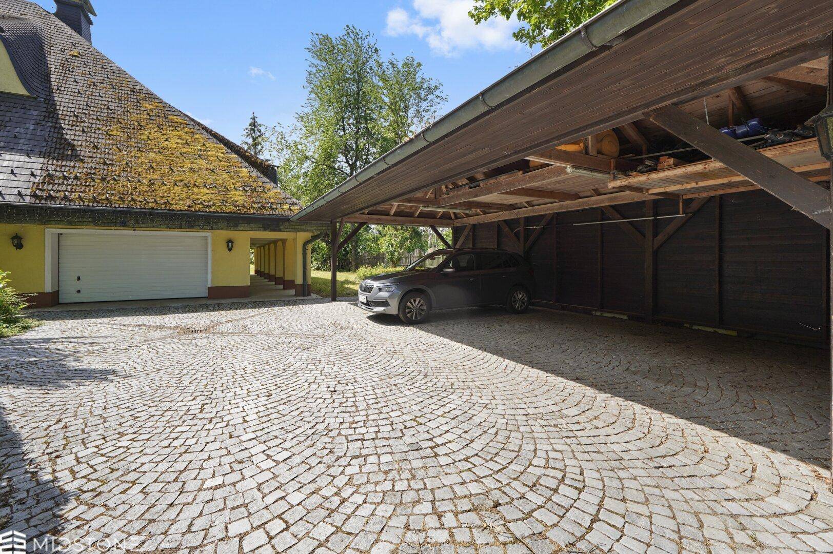 Überdachter Carport und Garage mit gepflasterter Zufahrt zum Anwesen.