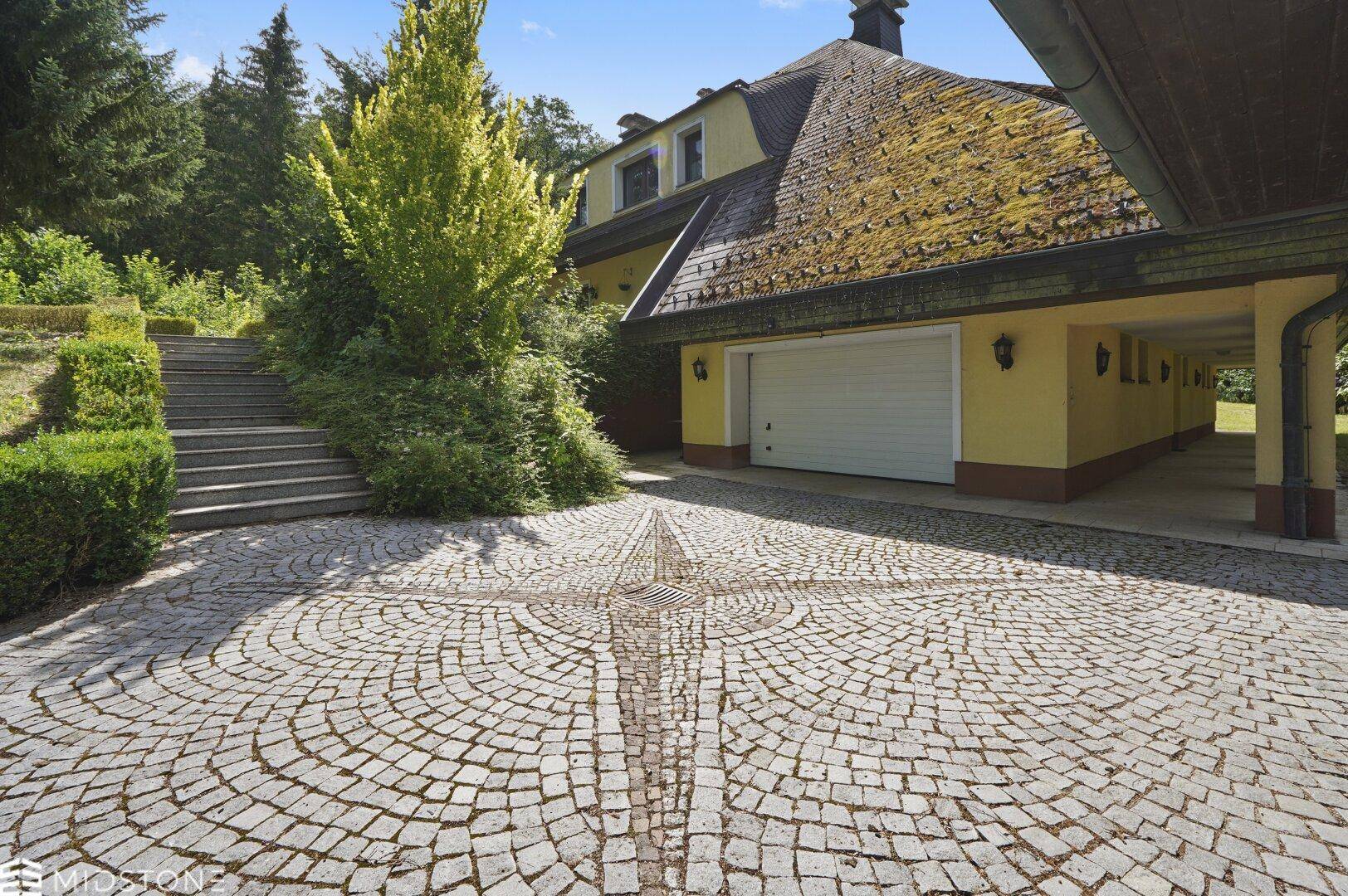 Zufahrt zum Anwesen mit Garage und kunstvoll gepflastertem Vorplatz.