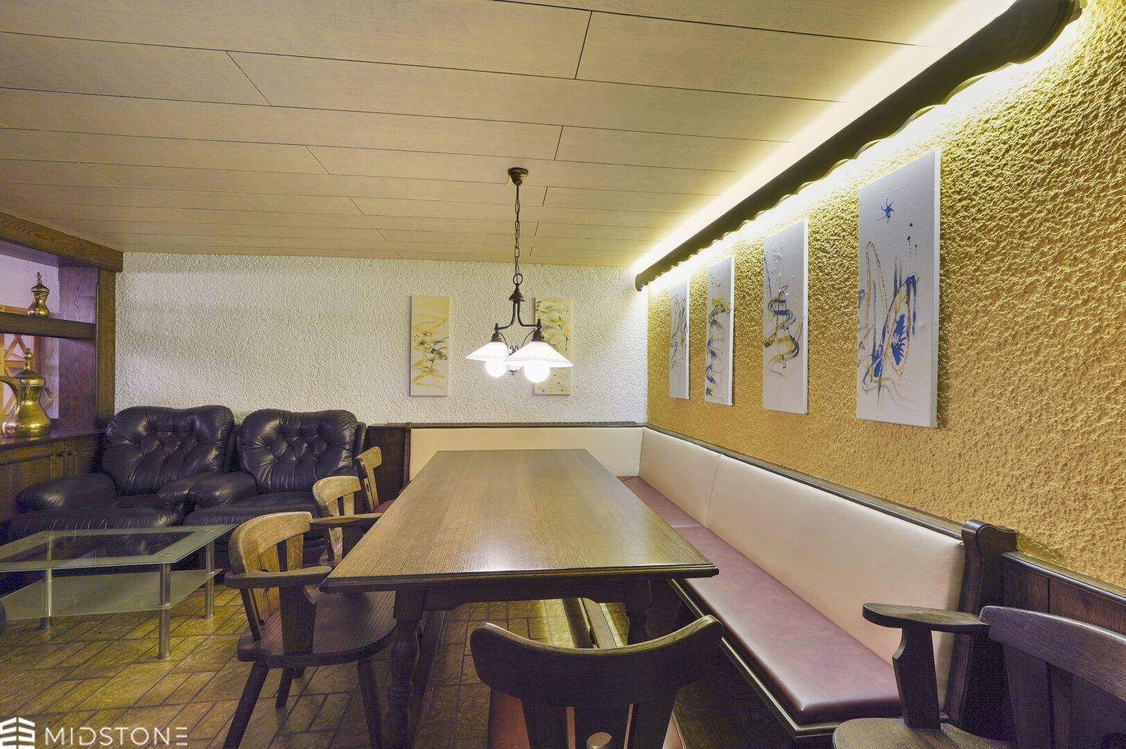 Rustikaler Essbereich mit langer Holztafel, Eckbank und Ledersofa, gemütlich beleuchtet.