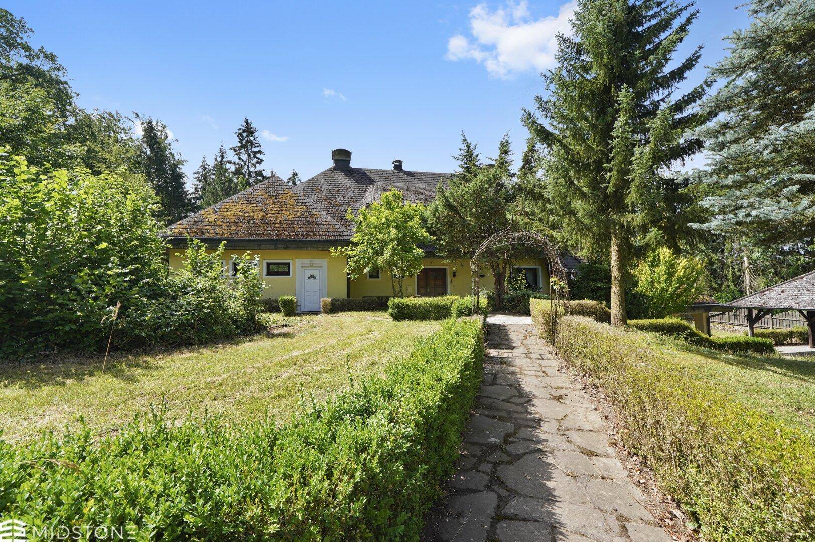 Vorderer Gartenbereich des Hauses mit Steinweg, Rasen und gepflegten Hecken unter blauem Himmel.