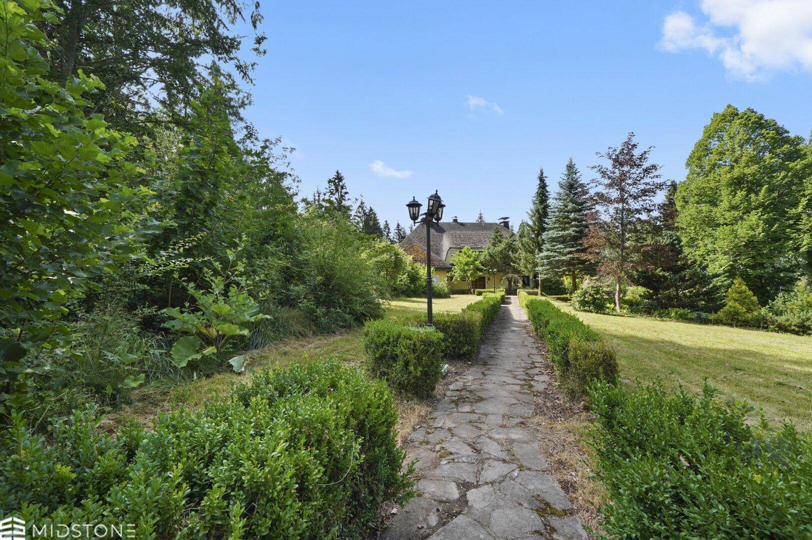 Steinweg führt durch den Garten zum Haus, gesäumt von Hecken und einer Laterne.