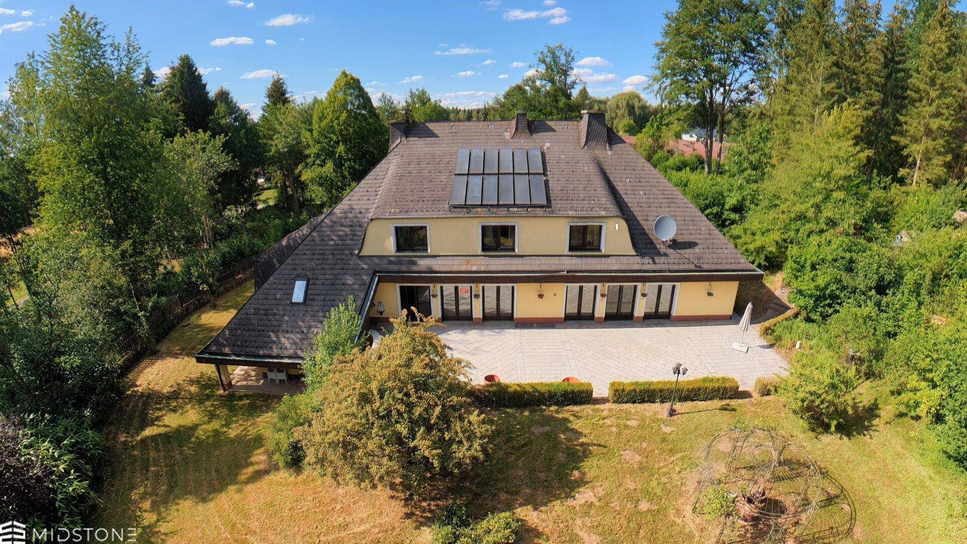 Luftaufnahme des Hauses mit großer Terrasse, Garten und Solarpaneelen auf dem Dach.