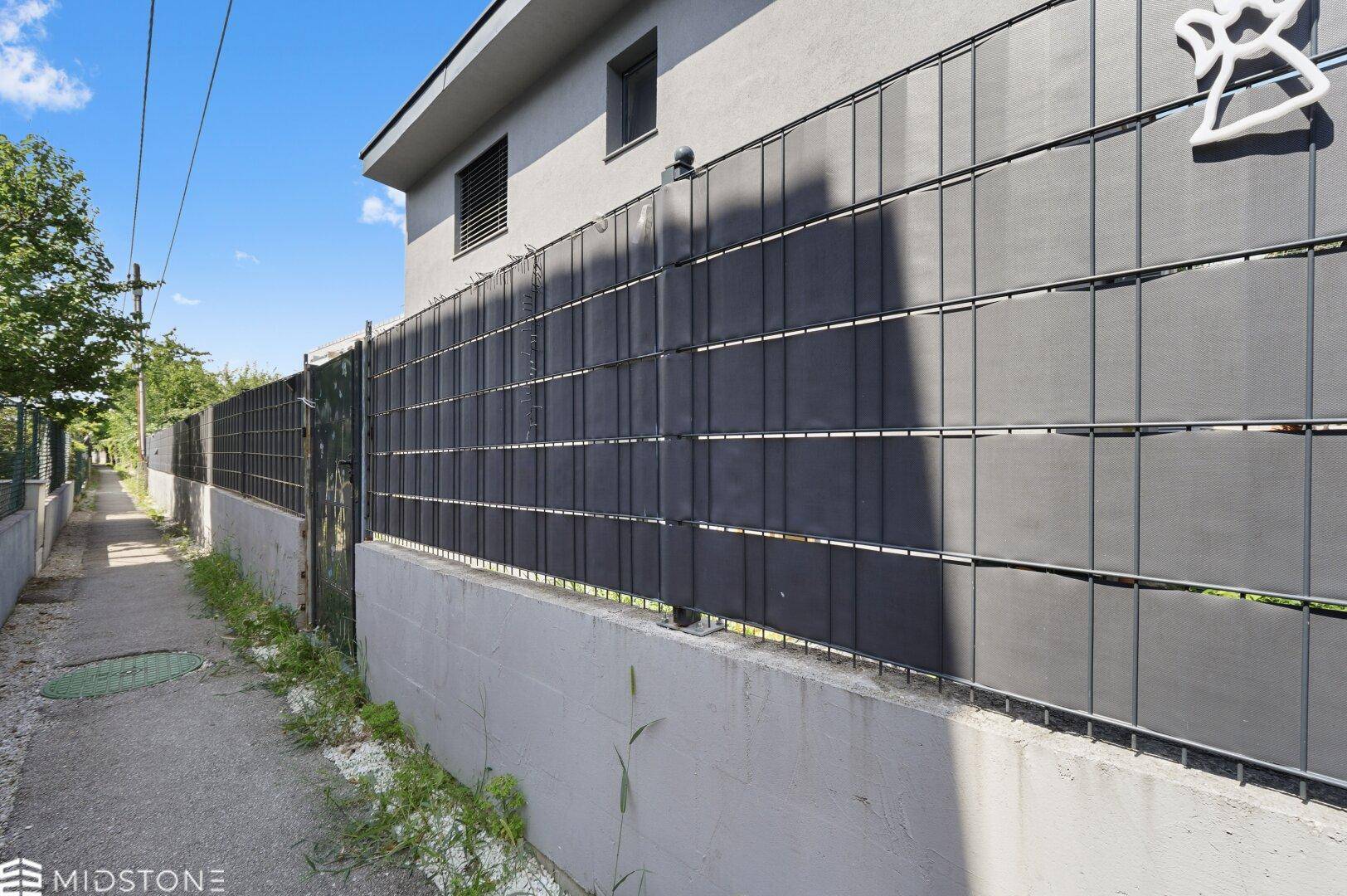 Seitenansicht des Hauses mit modernem Zaun und schmalem Weg.