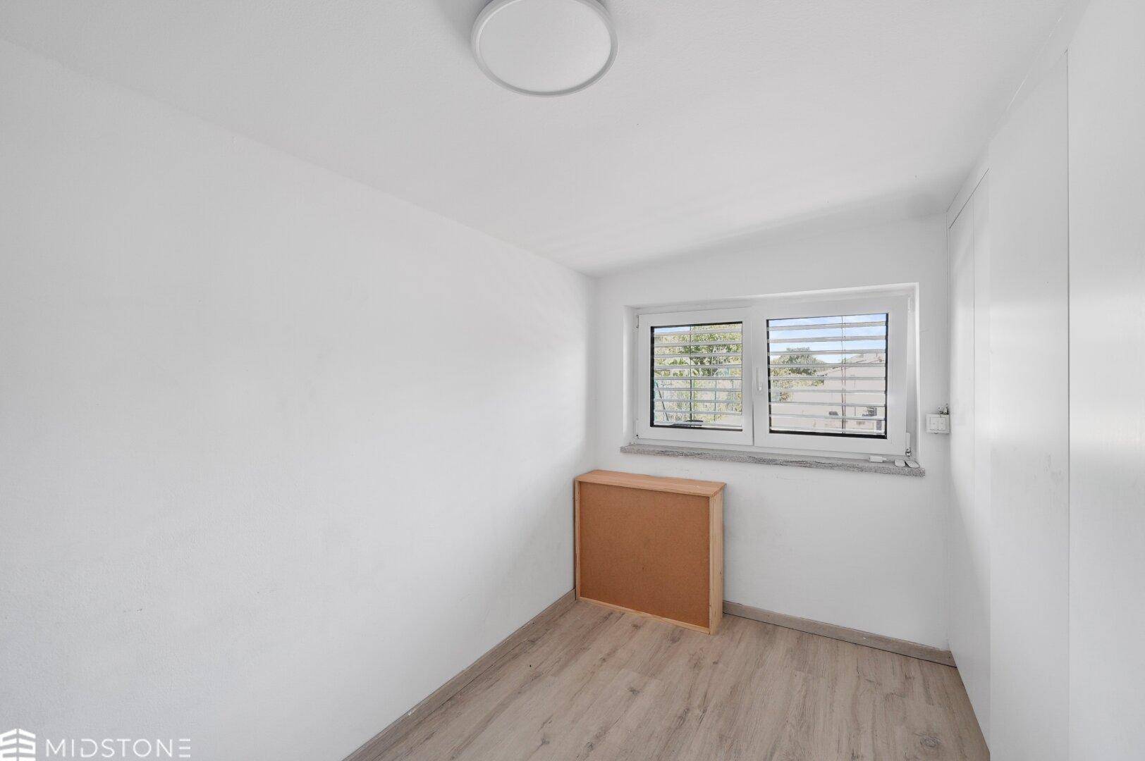 Kleines Schlafzimmer mit hellem Laminatboden und Fenster mit Blick ins Grüne.
