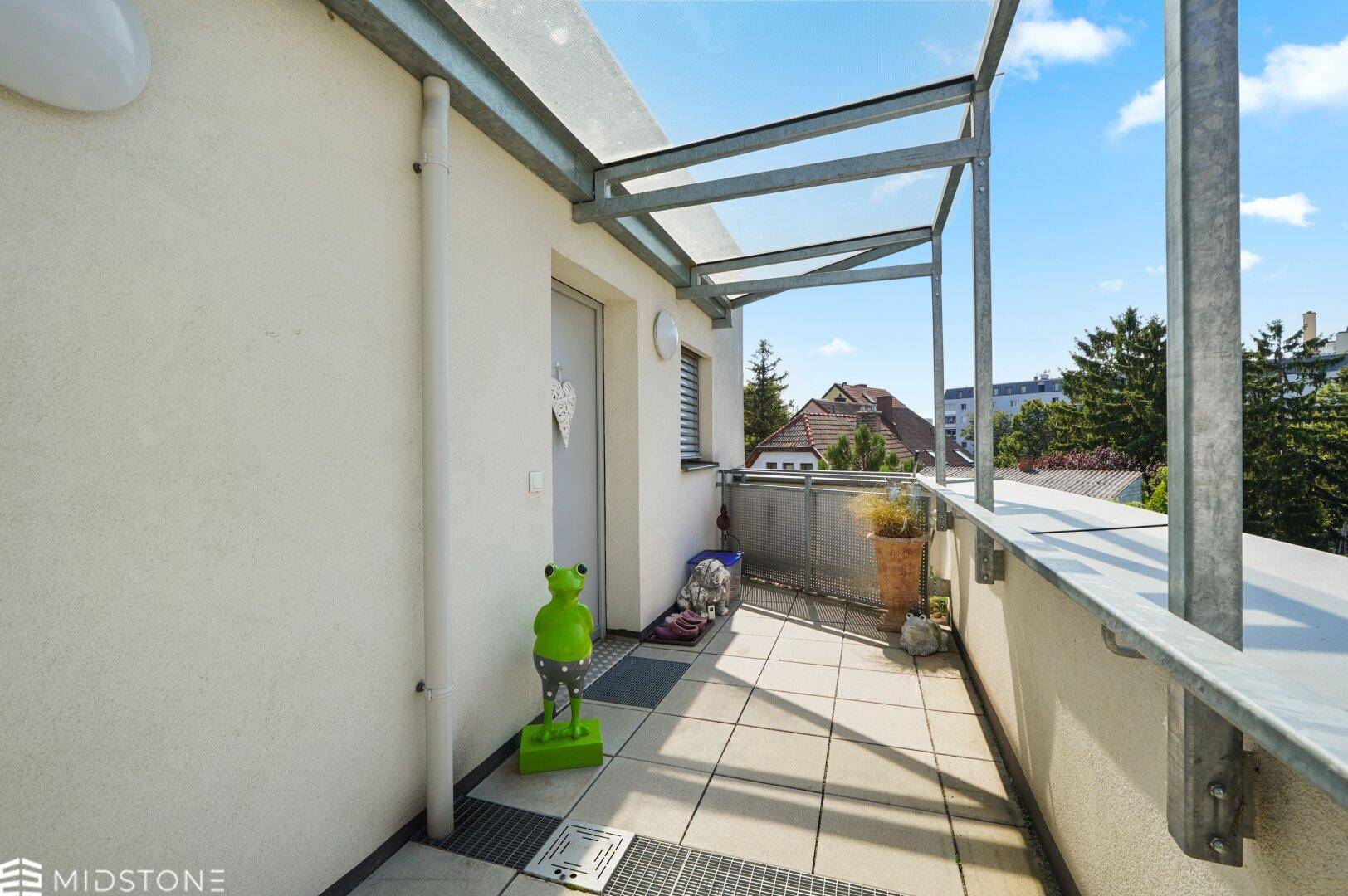 Heller Balkon mit Fliesenboden, Metallgeländer und Blick auf die umliegenden Häuser und Bäume.