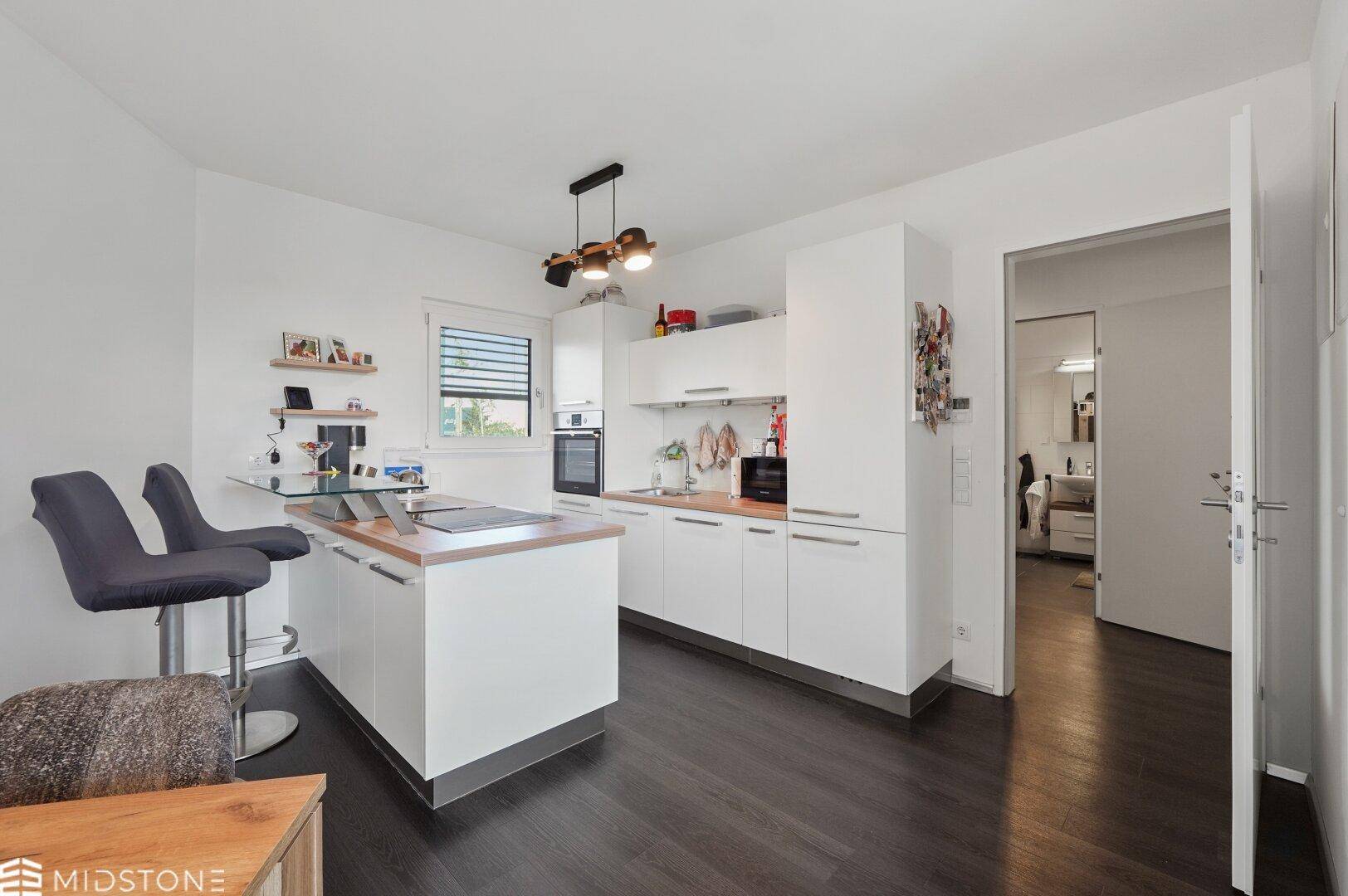 Moderne weiße Küche mit Kochinsel, Frühstücksbar und integrierten Geräten.