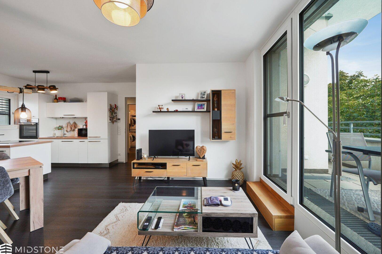 Heller Wohnbereich mit TV-Möbel, Couchtisch und großen Fenstern zum Balkon.