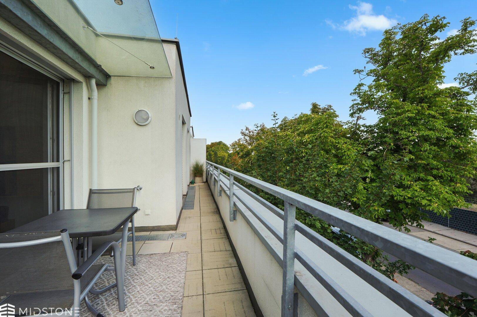 Langer Balkon mit Fliesenboden, Sitzgelegenheiten und grüner Aussicht.