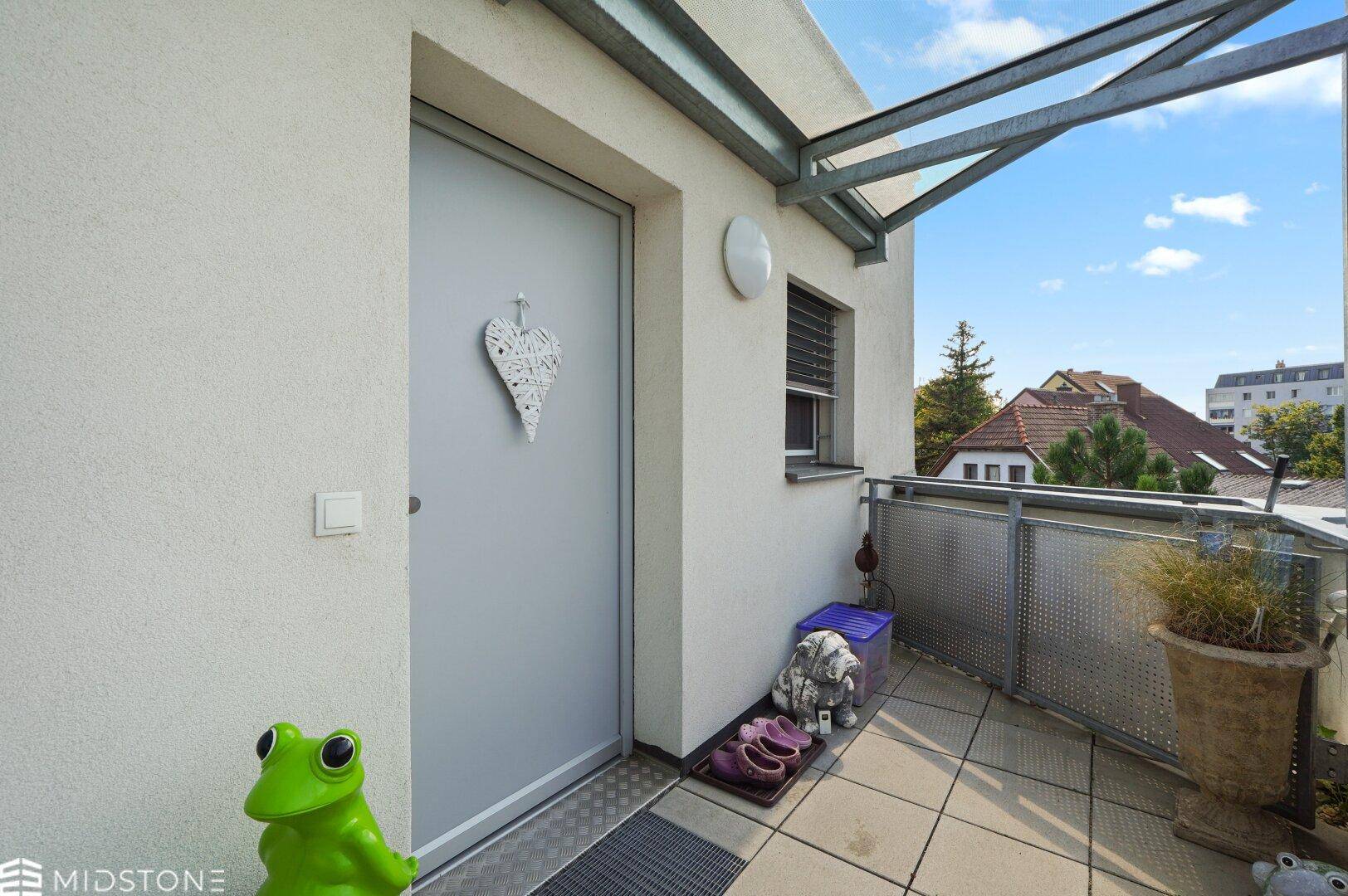 Eingangsbereich der Wohnung auf einem überdachten Außenbalkon mit Dekoration.