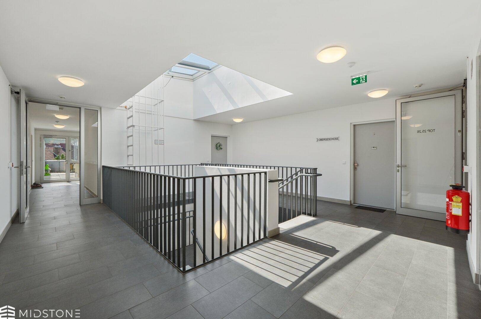 Geräumiger Flur im Gebäude mit Treppenhaus, Aufzug und viel Tageslicht.