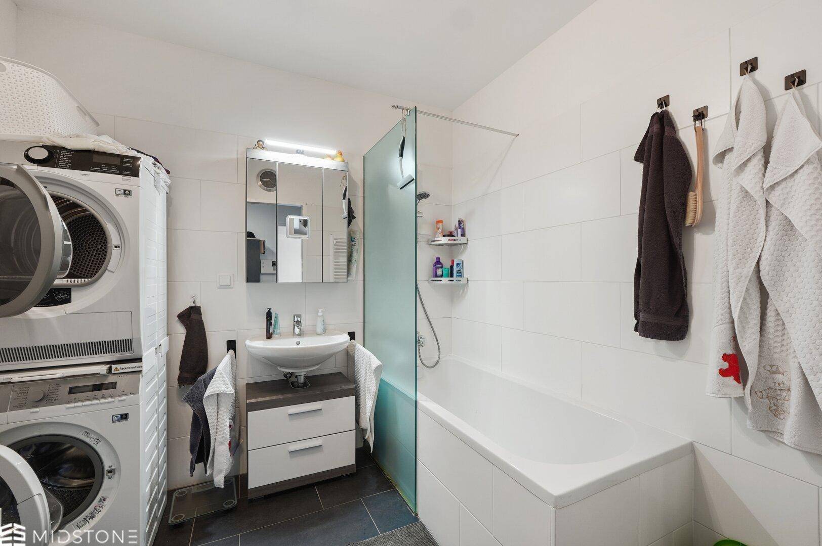 Modernes Badezimmer mit Badewanne, Duschbereich, Waschbecken und integrierten Waschmaschinen.