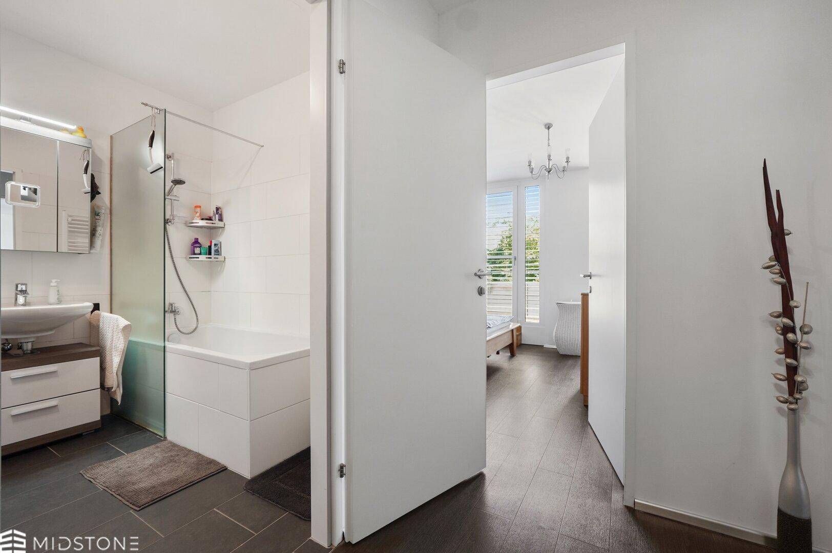 Heller Flur mit dunklem Boden, der zum Badezimmer und Schlafzimmer führt.