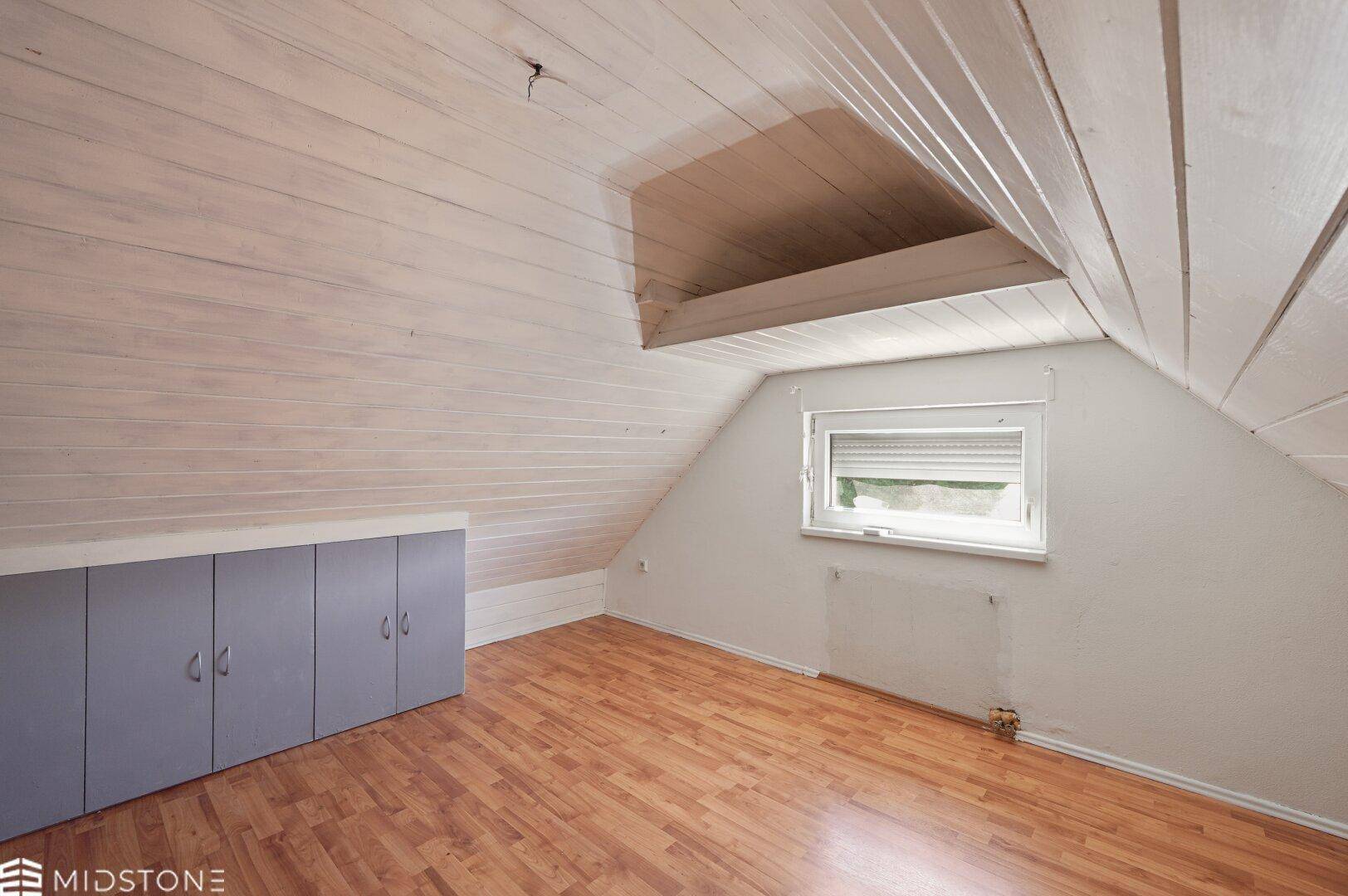 Dachzimmer mit Holzboden, Dachschräge und eingebauten Schränken für Stauraum.