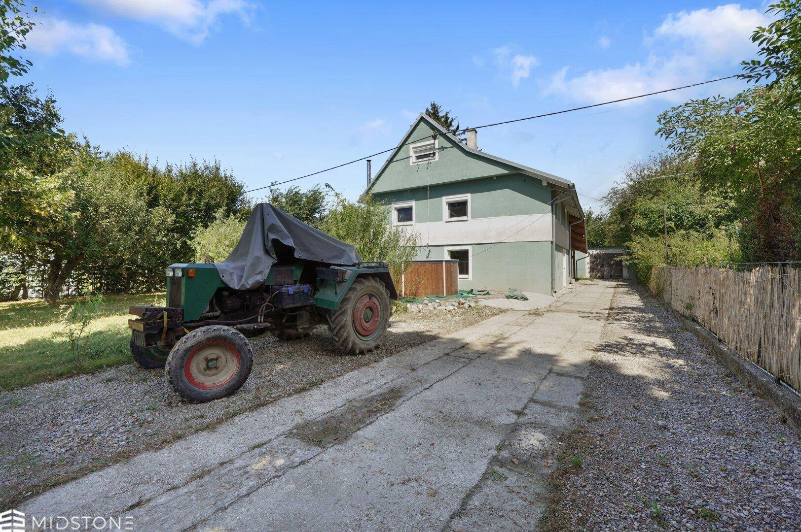 Ansicht des Hauses mit langer Auffahrt, einem Traktor und viel Grün im Vorgarten.