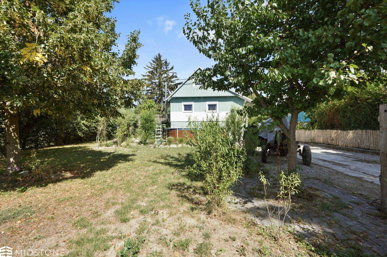 Großer Gartenbereich mit Rasenfläche, Bäumen und Blick auf das Haus und die Natur.