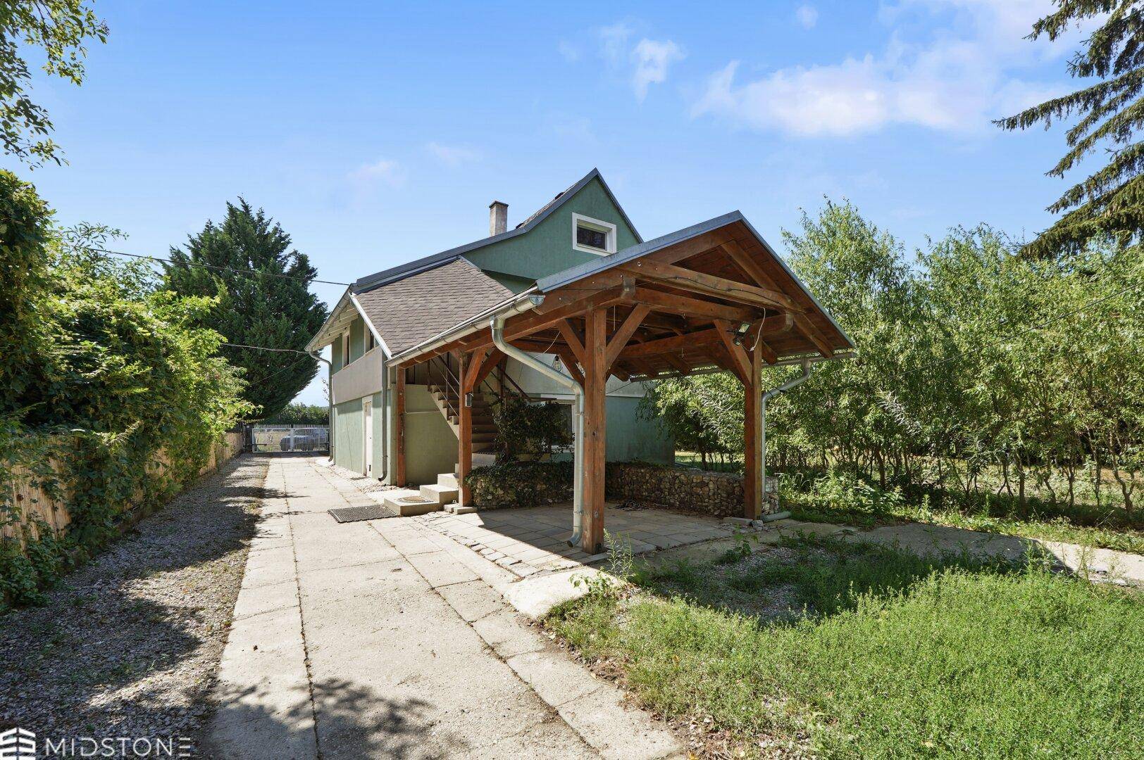 Hausansicht mit langem Zufahrtsweg und einem Holz-Carport im Grünen.