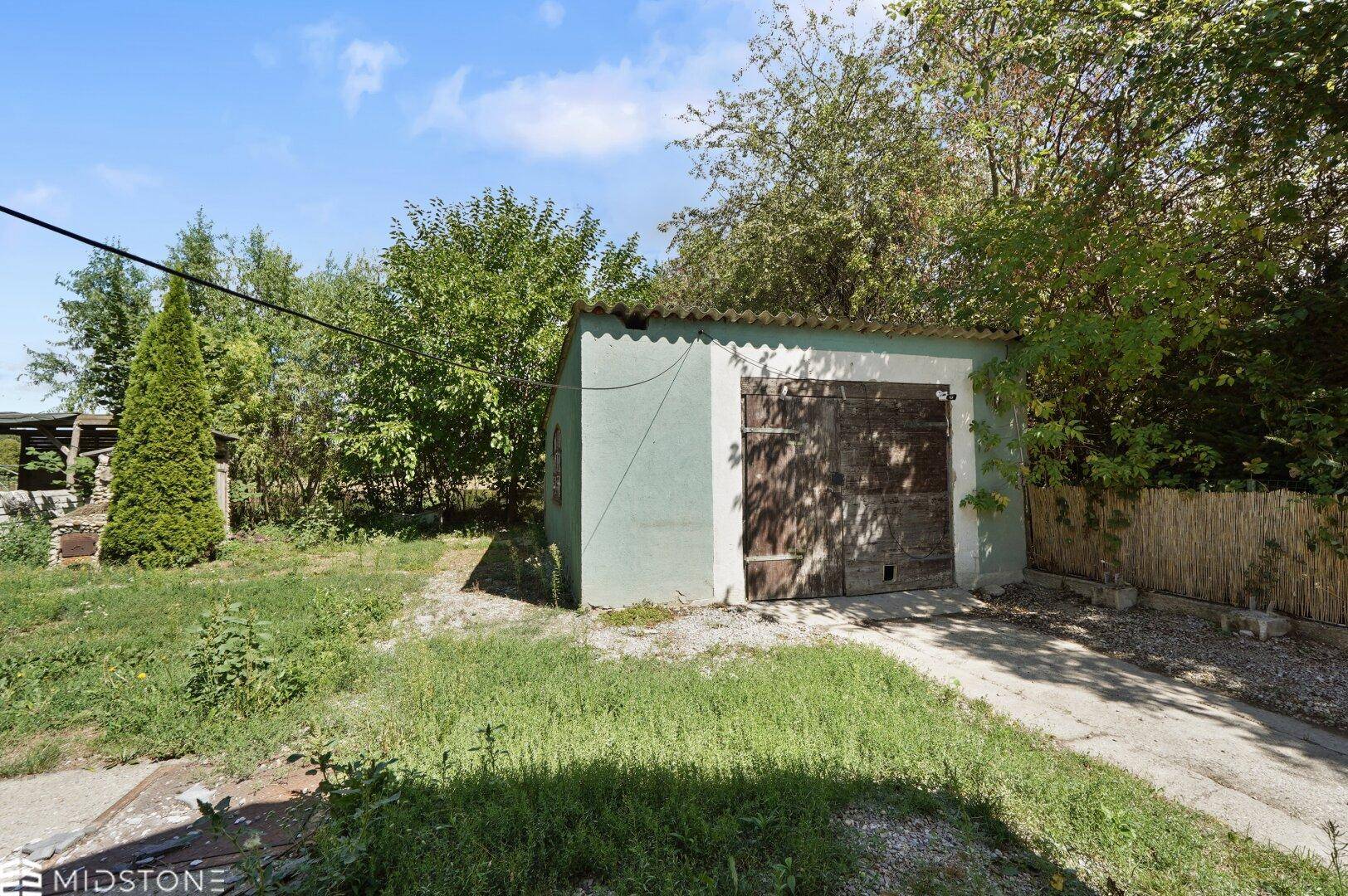 Freistehende Garage mit Holztor und umgebender Grünfläche auf dem Grundstück.