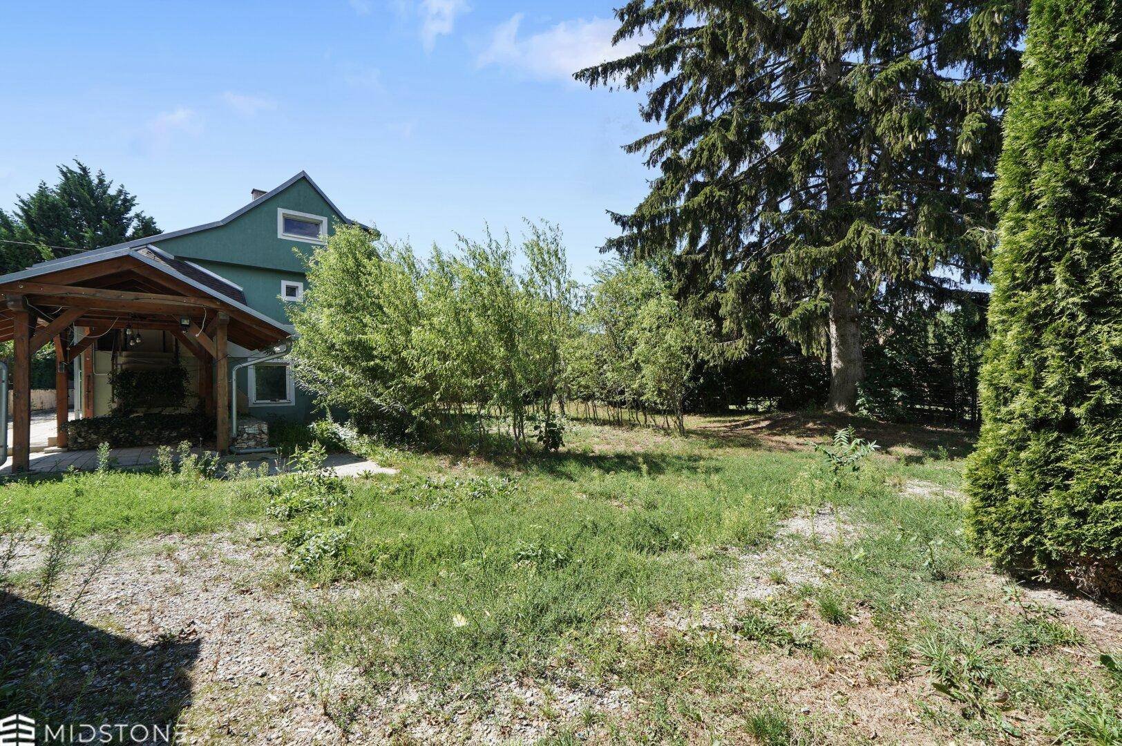 Weitläufiger Gartenbereich mit Bäumen und Blick auf das Haus und den Carport.