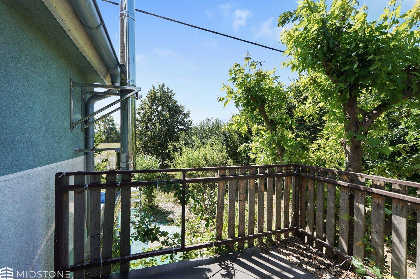 Balkon mit Holzbalkon und weitem Blick über die ländliche Umgebung und Bäume.