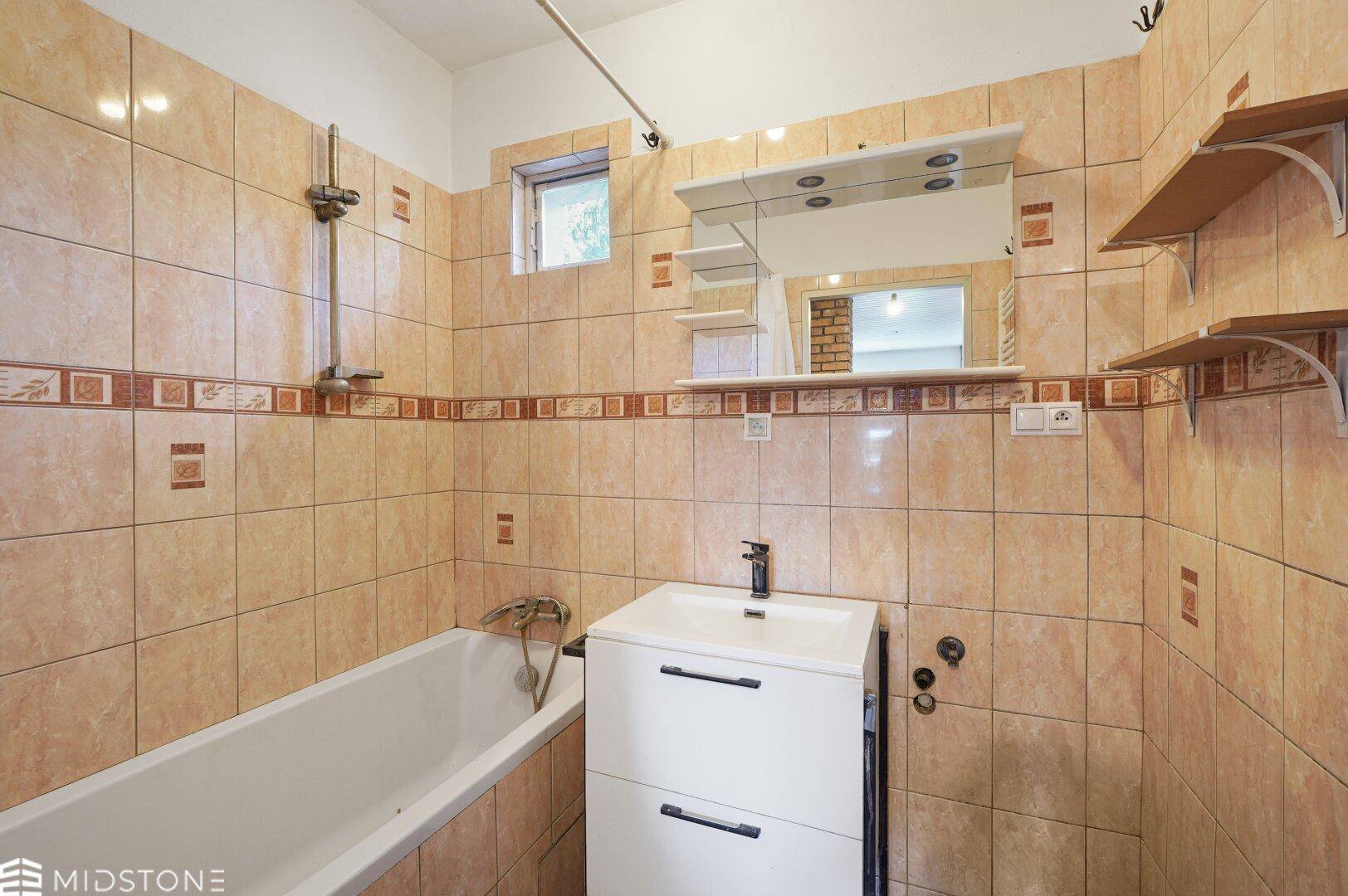 Badezimmer mit Badewanne, Waschbecken und gefliesten Wänden im 80er-Jahre-Stil.
