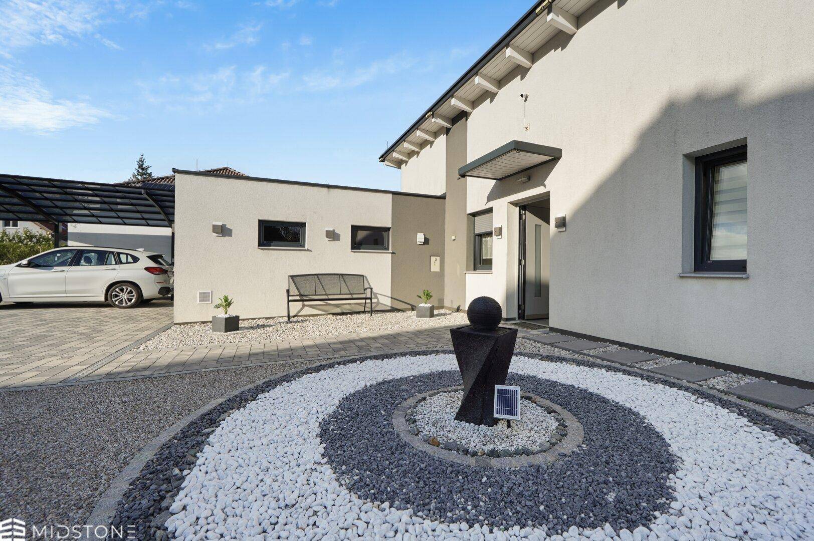 Eingangsbereich des Hauses mit modernem Steinkreis, Skulptur und einer Sitzbank im gepflegten Vorgarten.