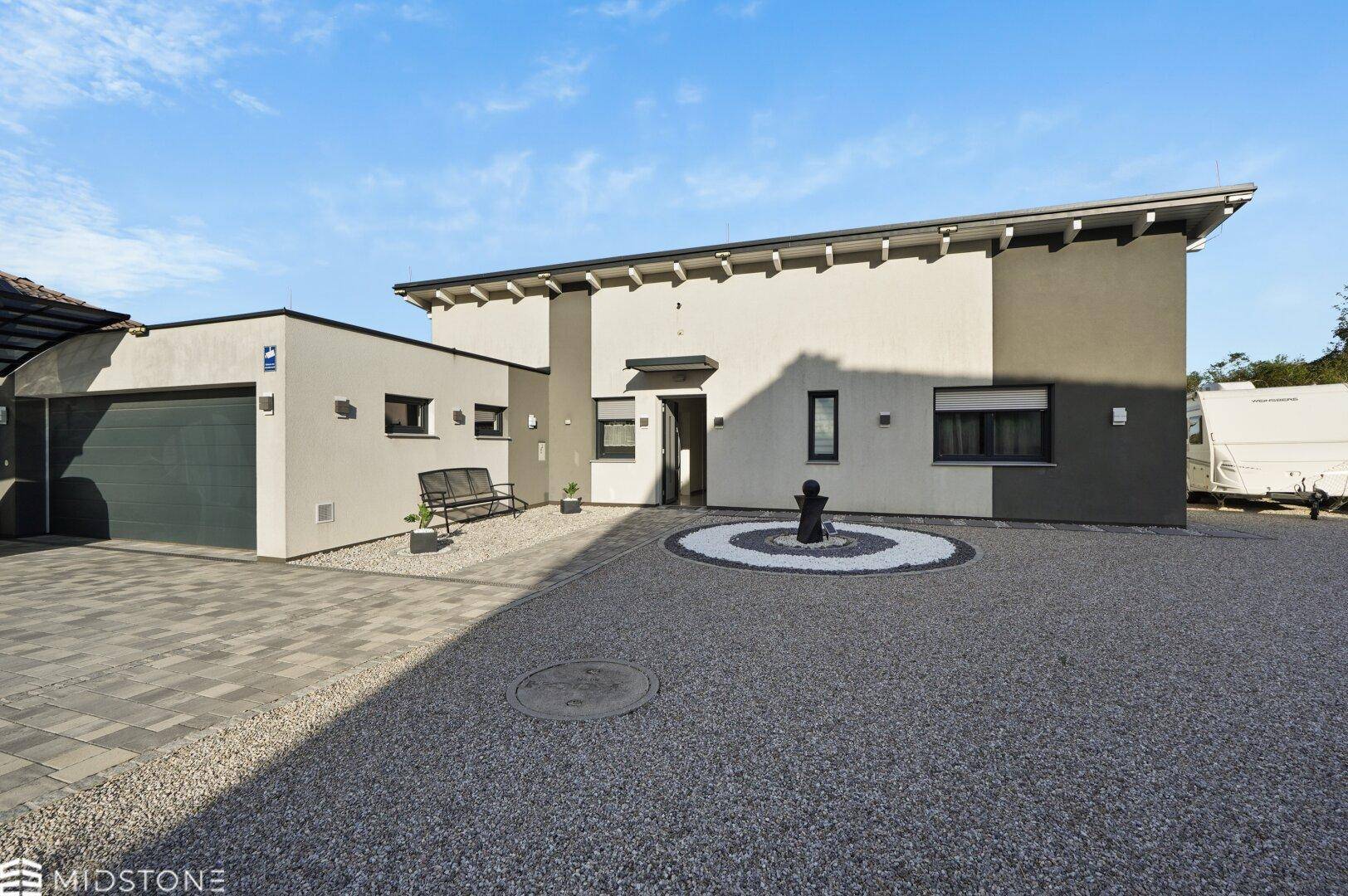 Vorderansicht des modernen Hauses mit Garage, Kiesauffahrt und einem dekorativen Steinkreis im Eingangsbereich.