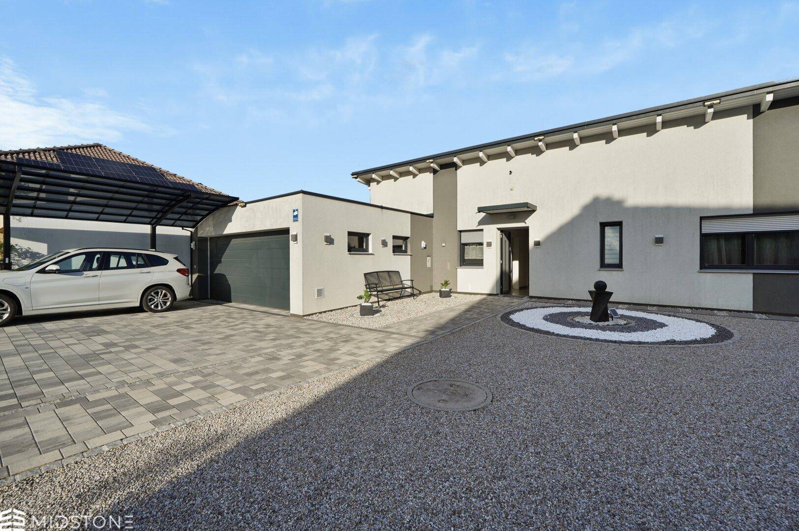 Modernes Einfamilienhaus mit Garage, Carport und gepflegter Kiesauffahrt unter strahlend blauem Himmel.