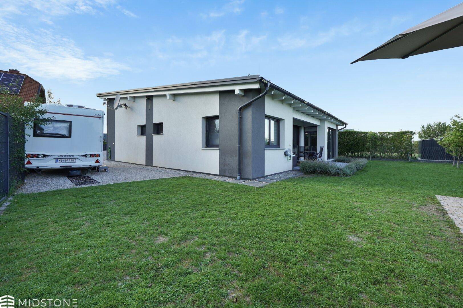 Rückansicht des modernen Hauses mit großer Rasenfläche und einem Wohnwagen auf dem Grundstück.