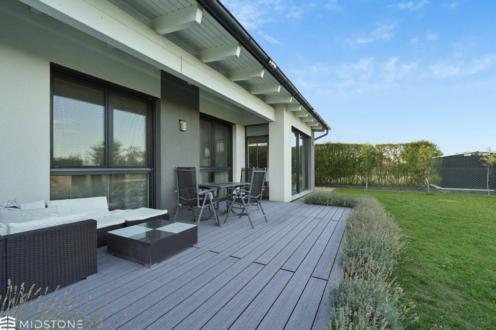 Geräumige Holzterrasse mit modernen Gartenmöbeln und direktem Zugang zur grünen Rasenfläche.