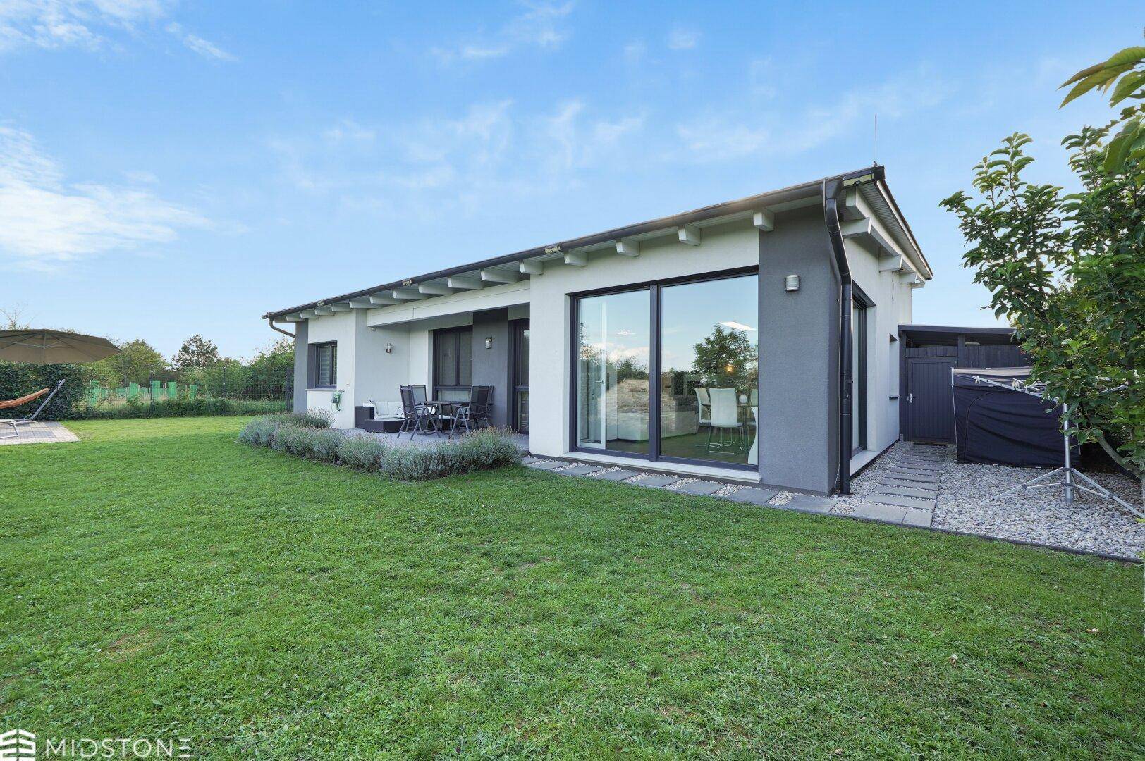 Rückansicht des modernen Hauses mit Rasenfläche, kleiner Terrasse und großen Fenstern zum Garten.