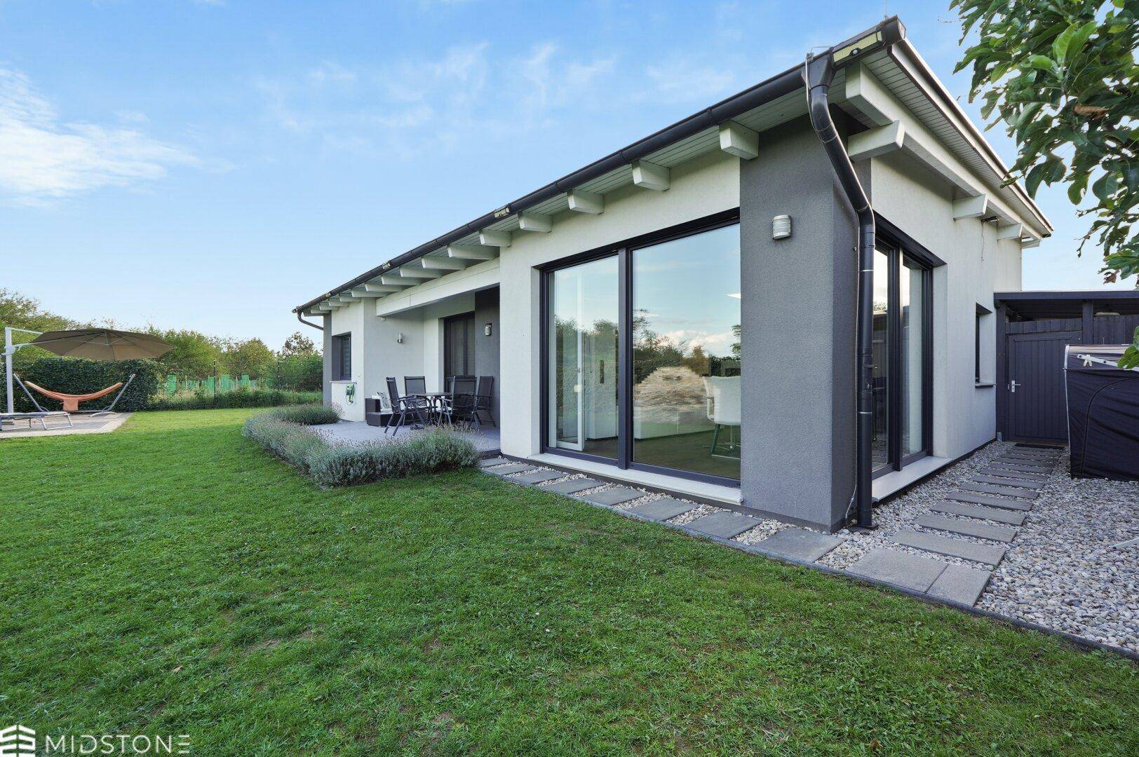 Modernes Haus von hinten mit weitläufigem Rasen, großen Fensterfronten und Blick ins Grüne.