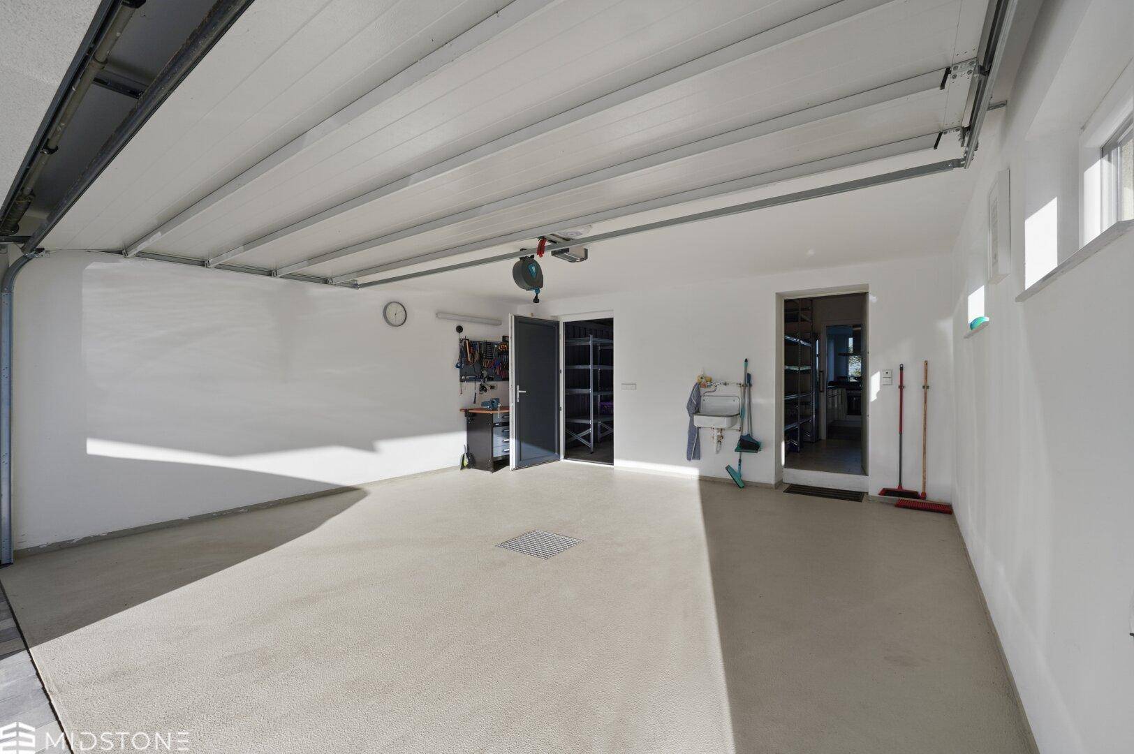 Geräumige Garage mit Betonboden, weißen Wänden und automatischem Garagentoröffner.