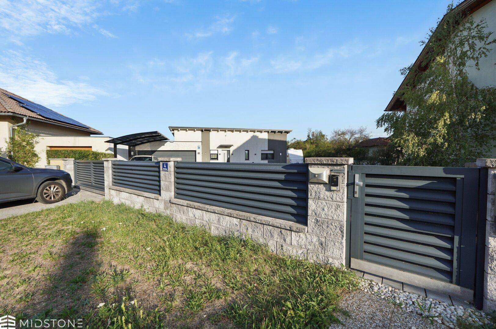 Moderner Zaun und Eingangstor des Grundstücks mit Blick auf das Haus im Hintergrund.