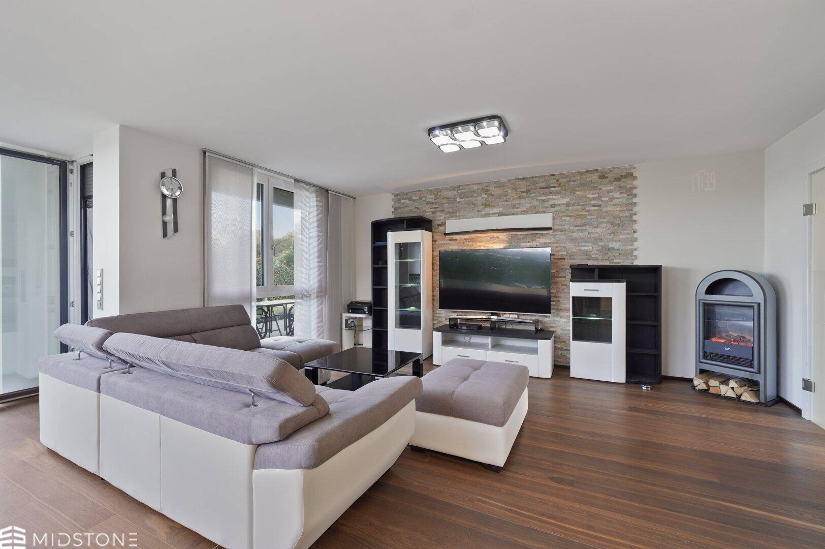 Gemütliches Wohnzimmer mit großem Sofa, Fernseher und modernem Kamin vor einer Steinwand.