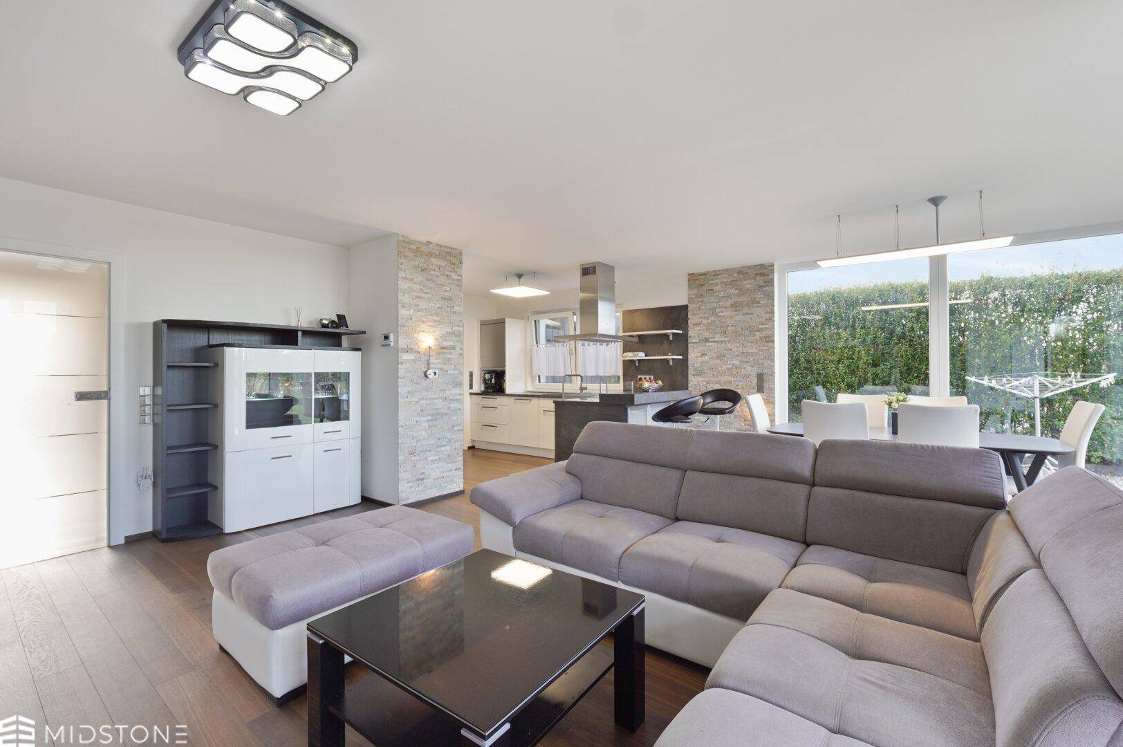 Offener Wohn-Essbereich mit gemütlichem Sofa und Blick auf die moderne Küche im Hintergrund.