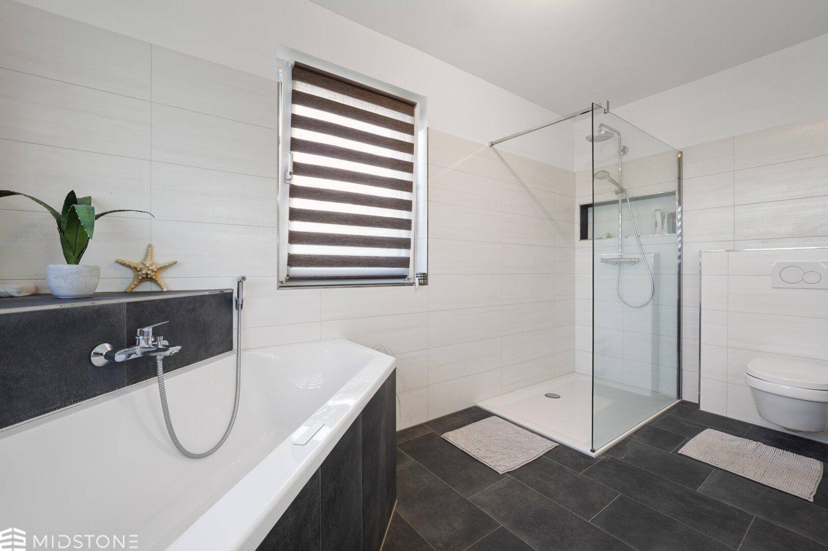 Modernes Badezimmer mit Eckbadewanne, ebenerdiger Dusche, Wand-WC und Fenster in hellen und dunklen Fliesen.
