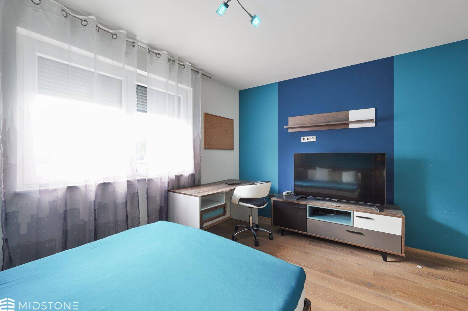 Helles Schlafzimmer mit blauer Wandgestaltung, TV-Möbel und Schreibtisch.