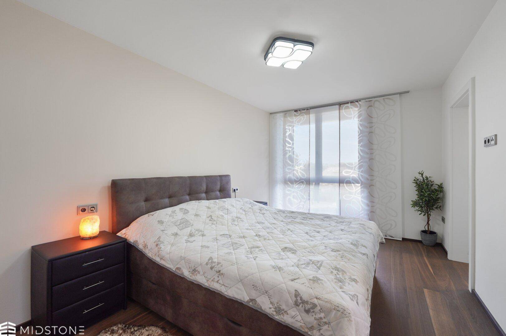 Gemütliches Schlafzimmer mit Doppelbett, Nachttisch und großem Fenster.